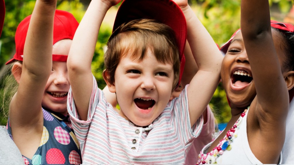 Photo of diverse group of children smiling with their hands overhead.